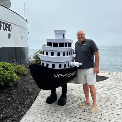Bryan Kasper posing with a Benson Ford Ship House mascot, next to the Ship House.